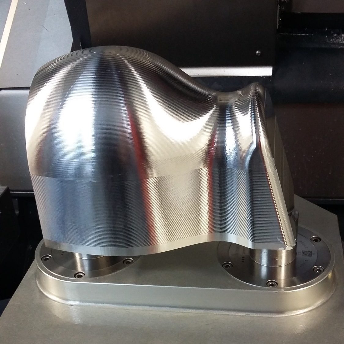 3d Aluminiumformteil Ein glänzendes, metallisches Bauteil mit geschwungenen Formen auf einer Maschine.